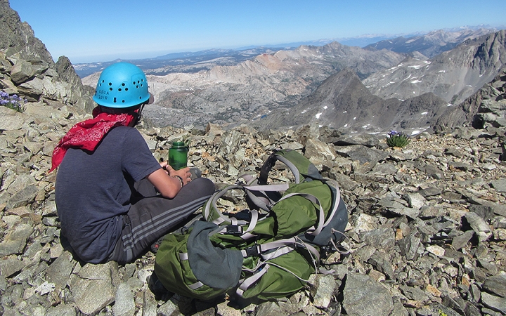 a person wearing a helmet rests on a rock and looks out over a vast rocky landscape